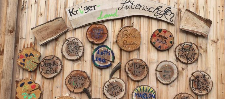 Eine Holzwand mit runden Holzscheiben auf welchen Namen von Kindern stehen, die eine Schafpatenschaft bei Kr&uuml;ger-Land haben.